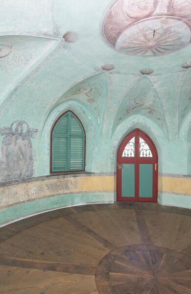 Historischer Innenraum mit hellblauer Gewölbedecke und Rundbogenfenstern.