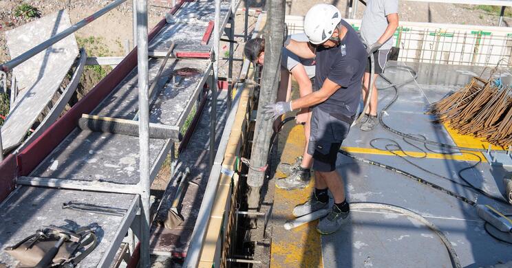Ein Bagger auf der Baustelle im Hofburg Garten; daneben steht eine Arbeiterin, im Hintergrund sind bewaldete Berge zu sehen.