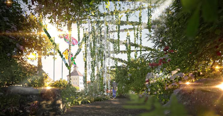 Gartenanlage mit üppiger Bepflanzung mit Windspiel und Hofburg im Hintergrund.
